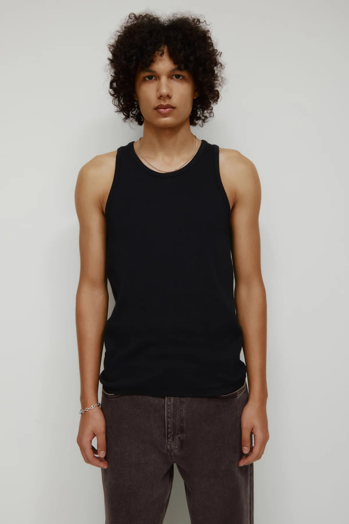 Person wearing a black tank top and dark pants against a plain background